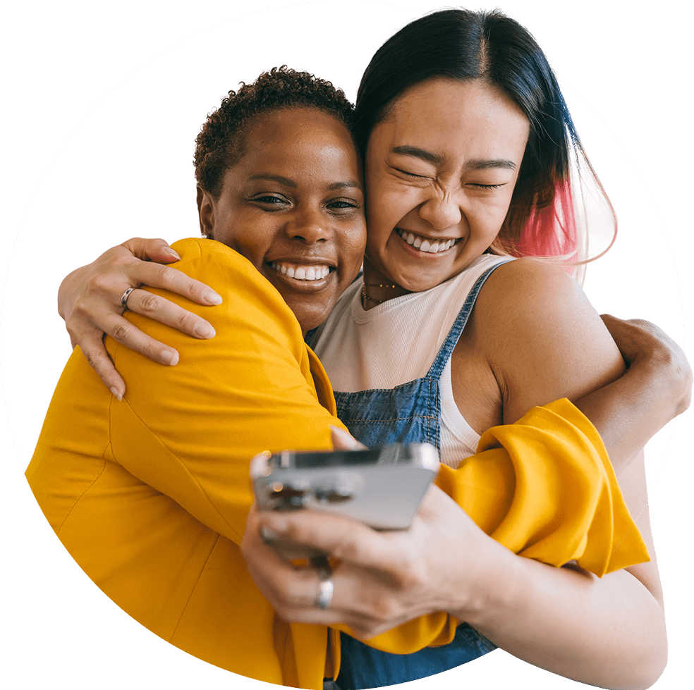 Two women hugging and smiling joyfully while taking a selfie together. 